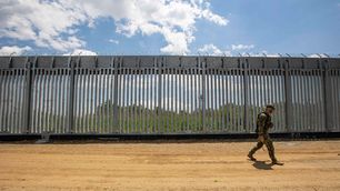 An armed military personnel is patroling along the fence, while there is a Turkish watchtower in the background behind the new fence. Greece is reinforcing the Greek Turkish borders.