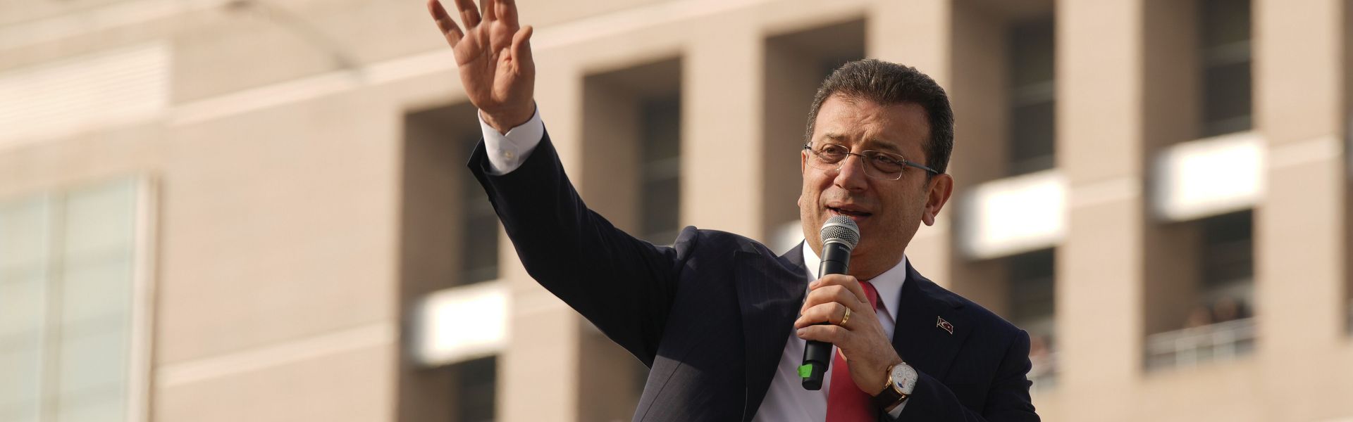 Ekrem İmamoğlu mit erhobener Hand und Mikrophon vor dem Gerichtsgebäude in Istanbul.